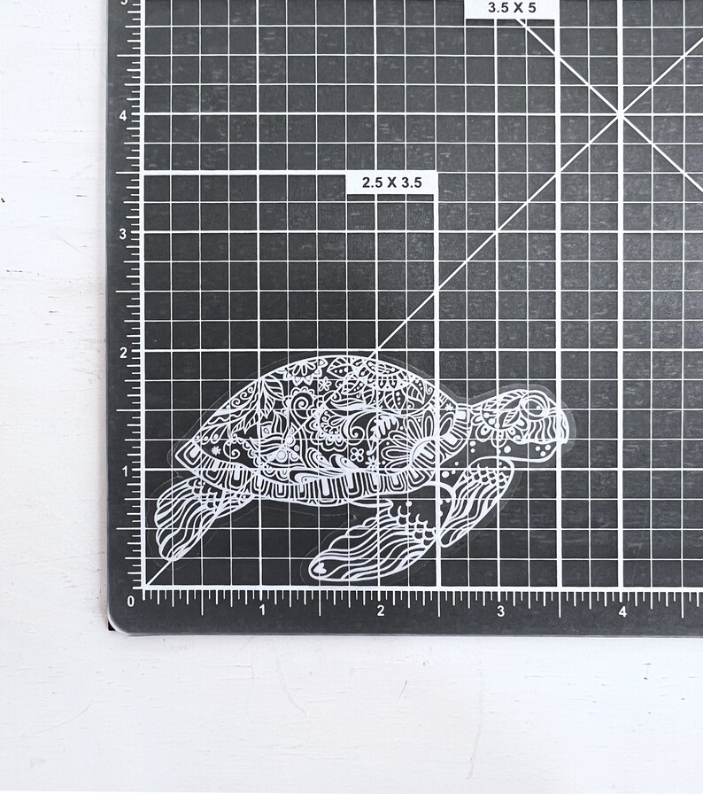 May include: A white, detailed, intricate, and ornate sticker of a sea turtle. The turtle is facing right and has a detailed shell and body.