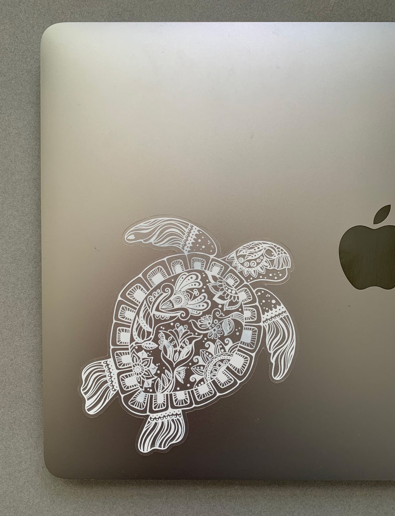 May include: A white vinyl sticker of a detailed, ornate, stylized turtle with a floral design on a silver laptop.