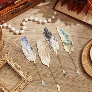 May include: Five gold metal feather bookmarks with different colored designs. The bookmarks have a chain with a small feather charm at the end.