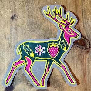 May include: A pink and green deer with yellow outlines, decorated with a strawberry, a flower, and feathers. The deer is standing on a gray background.