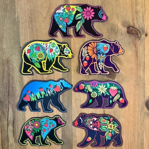 May include: Set of eight black bear silhouette stickers with colourful floral and strawberry designs. Each sticker features a different design with a combination of pink, yellow, green, blue, and purple flowers and strawberries.