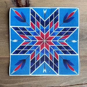 May include: Square blue fabric with a geometric star design. The star features red and blue diamond shapes, with red leaf-like accents and white arrow details. The fabric is likely a handkerchief or decorative cloth.