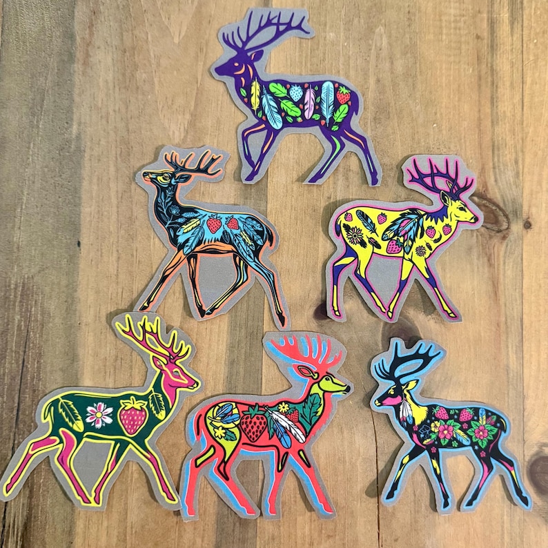 Op de afbeelding: Zes kleurrijke herten stickers met ingewikkelde patronen van veren, bladeren en aardbeien. De herten staan in verschillende poses en hebben verschillende gekleurde lichamen, waaronder paars, blauw, geel en rood.