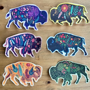 May include: Six decorative bison stickers with floral and geometric patterns. The stickers are in various colours, including blue, yellow, orange, and green. Each bison is outlined in white and has a unique design.