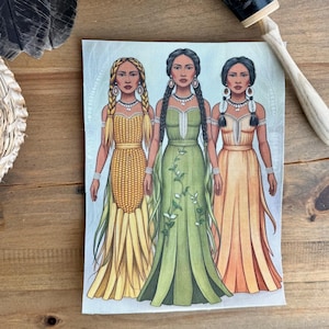 Peut inclure: Trois femmes en tenue traditionnelle amérindienne se tiennent côte à côte. La femme de gauche porte une robe jaune faite de feuilles de maïs. La femme du milieu porte une robe verte avec des vignes et des fleurs. La femme de droite porte une robe orange avec un motif perlé.