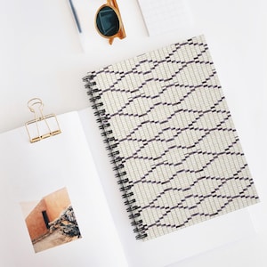 May include: A white spiral notebook with a black and white geometric pattern on the cover. The pattern is made up of small squares and rectangles.