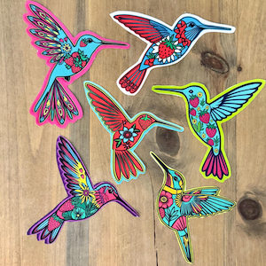 May include: Six colorful hummingbird stickers with intricate floral designs and strawberry accents. The stickers are on a wooden surface.