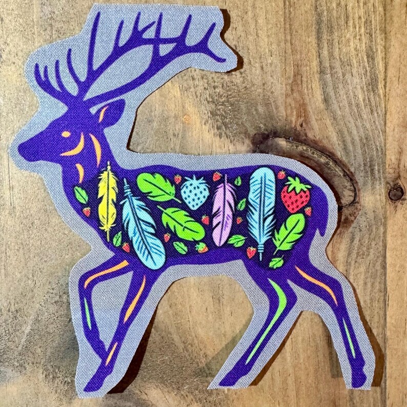 Op de afbeelding: Paarse hert silhouet met kleurrijke veren en aardbeien binnen de omtrek. Het hert staat op een houten achtergrond.