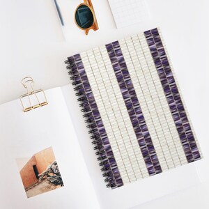 May include: A spiral bound notebook with a white and purple tiled pattern. The notebook has a white background with vertical stripes of purple tiles.