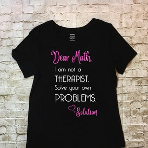 May include: Black t-shirt with the text "Dear Math. I am not a THERAPIST. Solve your own PROBLEMS. Solution" in pink glitter and white font. The shirt is a relaxed fit, XS size.
