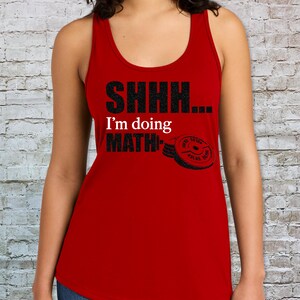 May include: A red tank top featuring the black text SHHH... and MATH, with the white text I'm doing in between. A black graphic of a weight plate is positioned next to the word MATH, completing the design on the front of the garment.