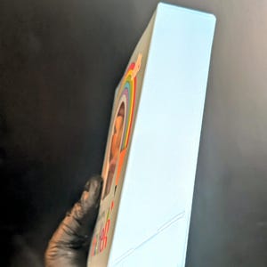 Puede incluir: Una caja azul claro con un arco&iacute;ris y una cara sonriente en la parte delantera. La caja tiene las palabras "Keep Calm and Carry On" impresas en la parte delantera.