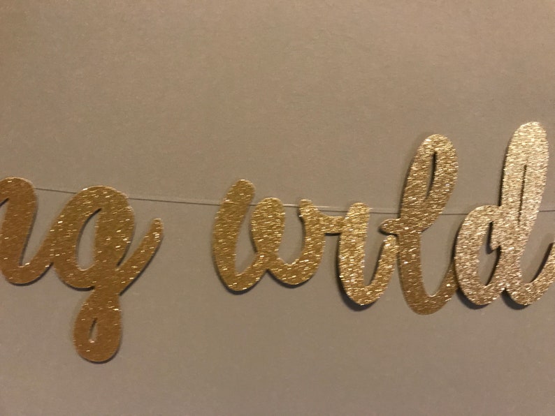 Puede incluir: Pancarta de purpurina dorada con las palabras "Hello World" en una fuente cursiva.