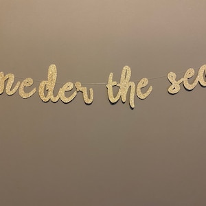 May include: Gold glitter banner with the words "under the sea" in a cursive font.