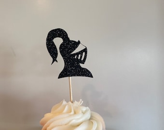 May include: A white cupcake with black glitter knight helmet cupcake topper. The cupcake is on a red plate.