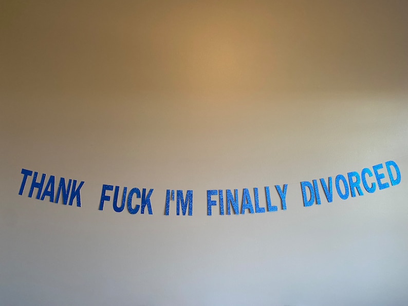 May include: Blue glitter letters spelling "THANK FUCK I'M FINALLY DIVORCED" on a white wall.