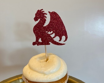May include: A cupcake with white frosting topped with a red glitter dragon cupcake topper.