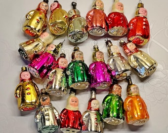 Puede incluir: Una colección de diecinueve adornos de vidrio vintage con forma de figuras que llevan abrigos y capuchas. Cada adorno presenta un acabado metálico en varios colores, incluyendo rojo, oro, verde, plata y rosa, con detalles faciales pintados.