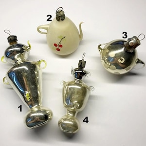 Könnte beinhalten: Eine Sammlung von vier Vintage-Weihnachtsschmuckstücken. Die Ornamente umfassen einen silbernen Samowar, eine Teekanne mit Kirschakzenten und zwei weitere silberfarbene Ornamente. Jedes Ornament hat eine Metallkappe und eine Schlaufe zum Aufhängen.