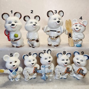 May include: A collection of nine white ceramic bear figurines, each numbered one through nine, depicting various sports and activities including tennis, weightlifting, skiing, and chess, all featuring a colourful belt detail.