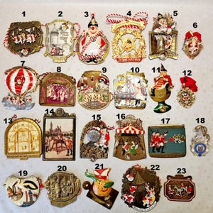 Peut inclure: Une collection de vingt-trois médailles décoratives en métal pour carnaval ou festival, numérotées, présentant des motifs en émail colorés, des personnages et du texte, suspendues par des cordelettes ou rubans, disposées sur un fond clair.