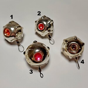 May include: Four vintage silver Christmas baubles with red centres. Each bauble has a unique shape with small bumps and a loop for hanging. The baubles are arranged on a white surface.