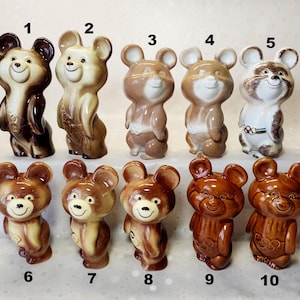 May include: Ten ceramic bear figurines arranged in two rows, numbered one through ten. Each bear features a smiling face, rounded ears, and a glossy finish in various shades of brown, tan, and white, with some displaying Olympic ring motifs.