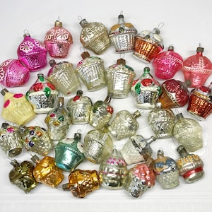 Könnte beinhalten: Eine Sammlung von Vintage-Weihnachtsbaumschmuck aus Glas in verschiedenen Formen und Farben, darunter Körbe, Cupcakes und Glocken. Der Schmuck ist mit filigranen Details verziert und hat eine matte Oberfläche.
