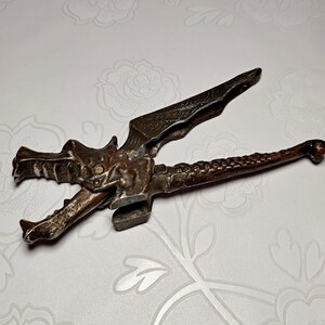 May include: A vintage metal nutcracker in the shape of a dragon. The dragon's head forms the jaws, and the wings serve as the lever. The nutcracker has a detailed, textured design and a dark, aged finish.
