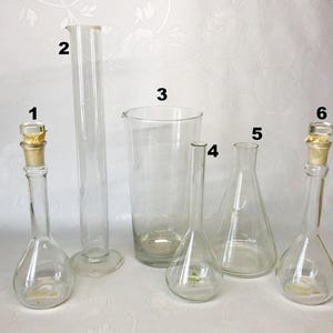 May include: A set of six clear glass laboratory beakers and flasks, some with stoppers. The beakers and flasks are of varying sizes and shapes.