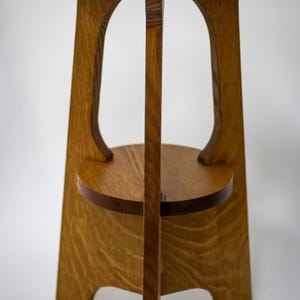 May include: A handcrafted wooden side table with a round top and a lower shelf. The table has a warm, natural wood finish and a unique design with curved supports. The table is approximately 28 inches tall.