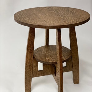 May include: A round, wooden end table with a lower shelf. The table is made of dark brown wood with a natural grain pattern.
