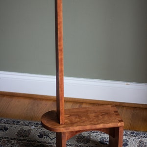 May include: A wooden step stool with a tall back support. The stool is made of cherry wood and has a natural finish. The stool is standing on a patterned rug.