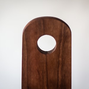 May include: A dark brown wooden chopping board with a circular hole in the centre. The board is made from natural wood with a smooth finish.