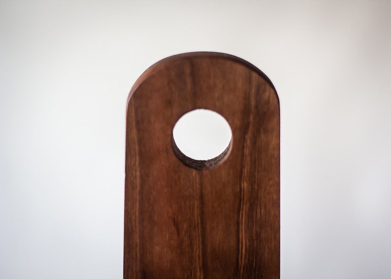 May include: A dark brown wooden chopping board with a circular hole in the centre. The board is made from natural wood with a smooth finish.
