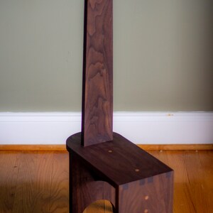 May include: A dark brown wooden step stool with a tall back and a circular cutout in the top. The stool has a simple, rustic design.