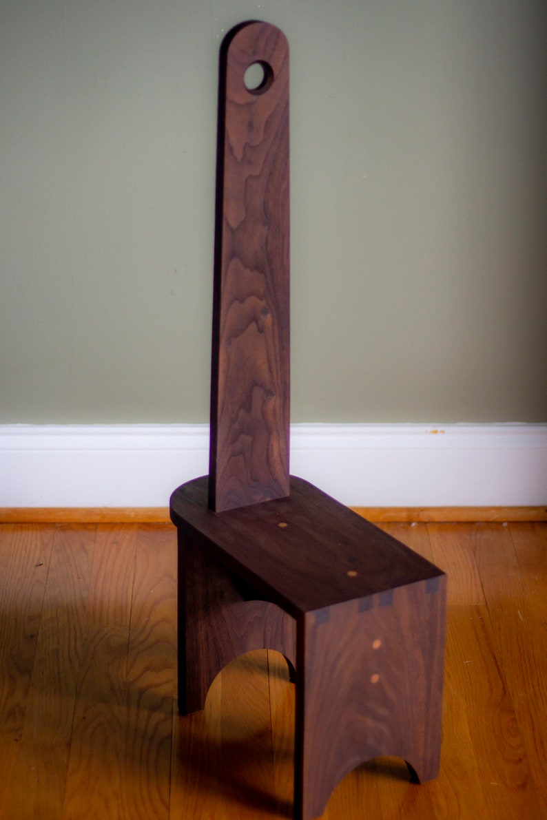 May include: A dark brown wooden step stool with a tall back and a circular cutout in the top. The stool has a simple, rustic design.