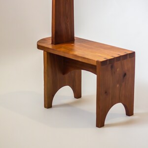 May include: A wooden stool with a tall back and a simple design. The stool is made of natural wood with a warm brown colour.