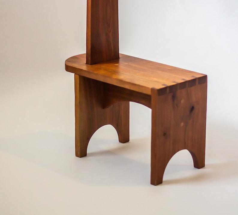 May include: A wooden stool with a tall back and a simple design. The stool is made of natural wood with a warm brown colour.