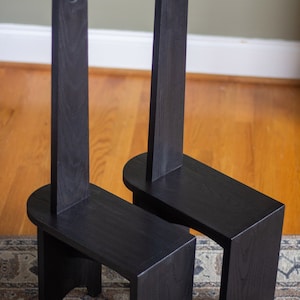 May include: Two black wooden chairs with tall backrests and rounded seats. The chairs are on a patterned rug.