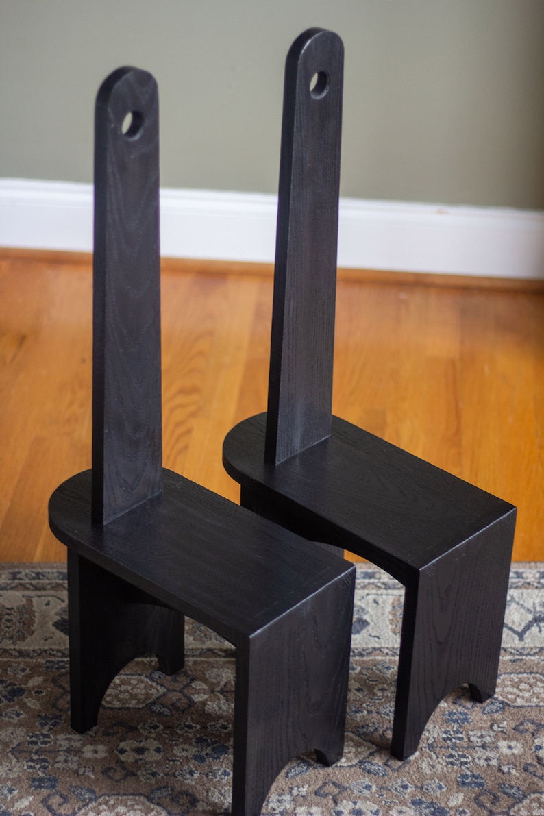 May include: Two black wooden chairs with tall backrests and rounded seats. The chairs are on a patterned rug.
