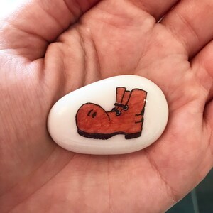 May include: A white painted rock with a brown boot drawn on it.