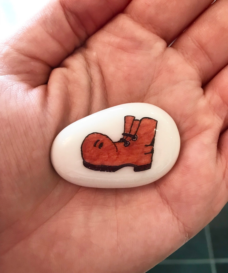 May include: A white painted rock with a brown boot drawn on it.