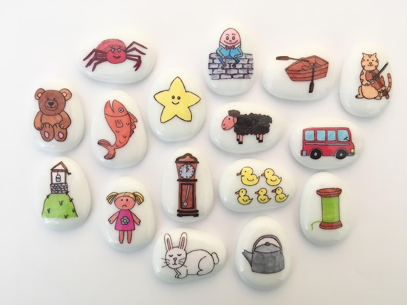May include: A set of 15 painted white stones with various illustrations, including a spider, a fish, a star, a sheep, a bus, a spool of thread, a clock, a teapot, a rabbit, a doll, a well, a boat, a cat, a bear, and an egg.