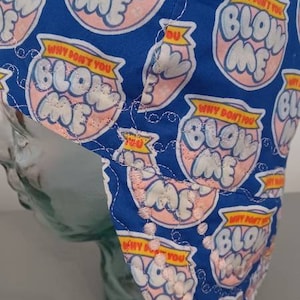 May include: Blue fabric cap with a repeating pattern of pink and white text that reads "BLOW ME" and "WHY DON'T YOU". The cap is stitched with white thread.