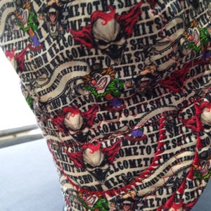 May include: A white fabric hat with a red, black, and green pattern. The hat has the text "Welcome to the Shit Show" repeated in a circular pattern.