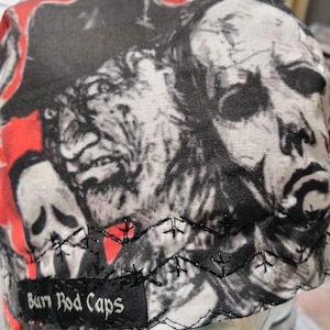 May include: A black and white skull and crossbones design on a red, white, and black baseball cap. The cap has a black label that says "Burn Rod Caps".