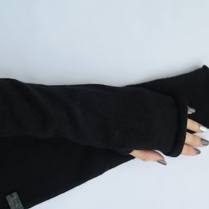 May include: A pair of black fingerless gloves made of a soft, knitted fabric. The gloves are long and extend past the wrist.