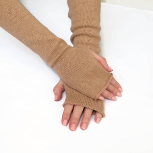 May include: A pair of brown fingerless gloves made of soft knit fabric. The gloves are worn on a person's hands, with the fingers exposed.