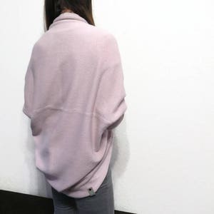 May include: A soft, pale pink, oversized sweater with a draped design. The sweater is made of a fuzzy, knit fabric.